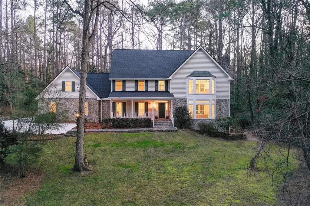 Traditional-style home with covered porch, stone siding, roof with shingles, and a front yard