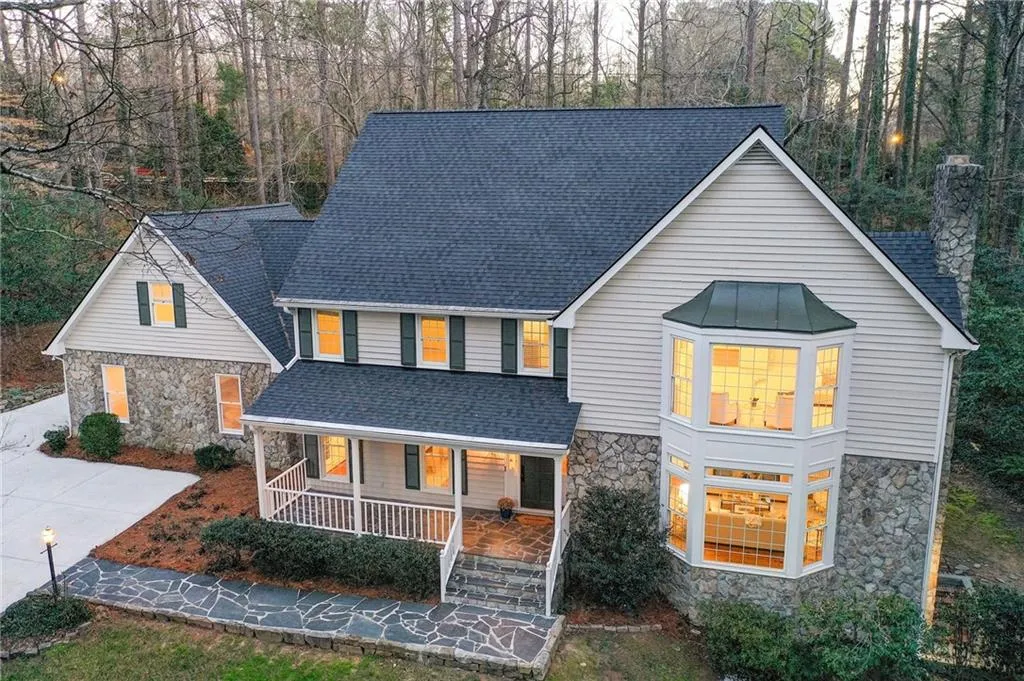 View of front of property with stone siding, a porch, roof with shingles, and a chimney