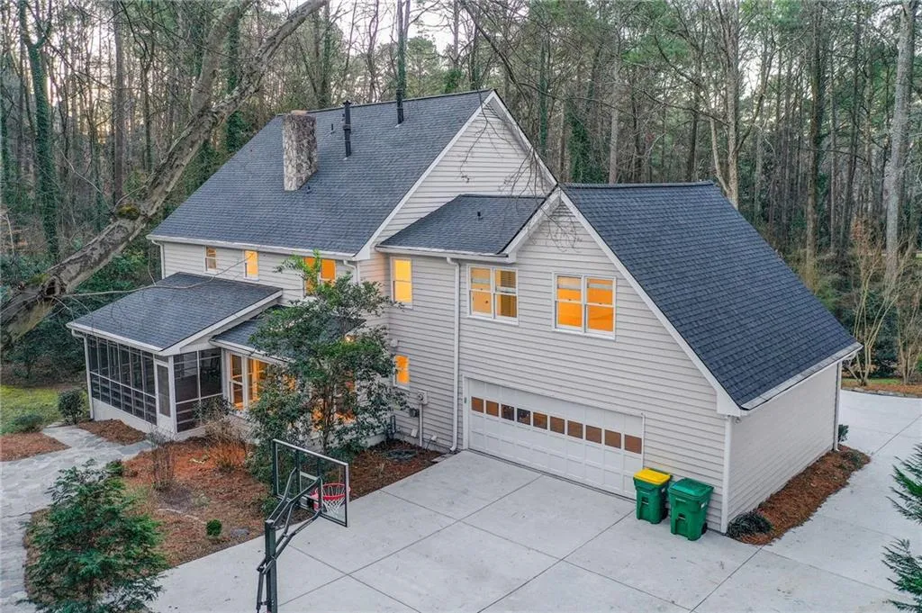 View of front of house with a shingled roof, an attached garage, a sunroom, driveway, and a forest view