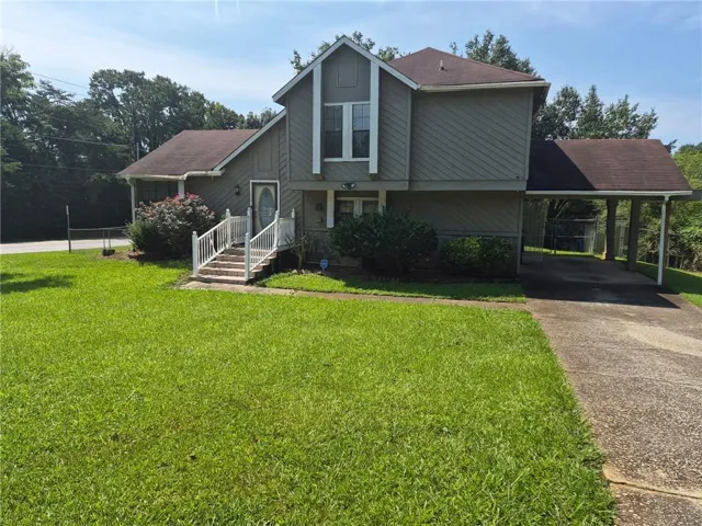 Exterior featuring a front entry with white railings, a covered carport, and a verdant lawn