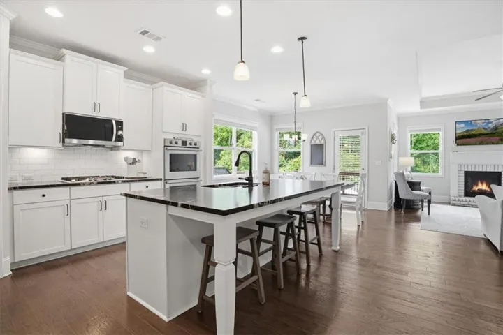 Kitchen featuring white cabinetry, dark countertops, a large island with seating, stainless steel appliances, and wood-finish flooring