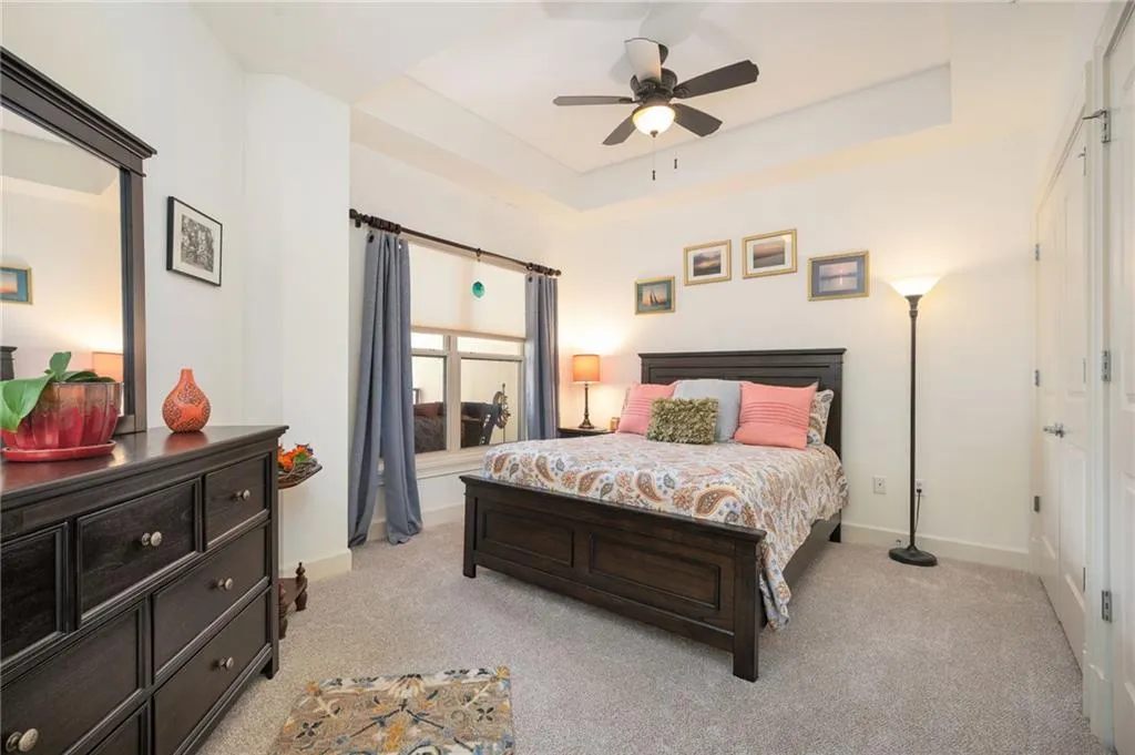 Bedroom with a tray ceiling, light colored carpet, baseboards, and ceiling fan