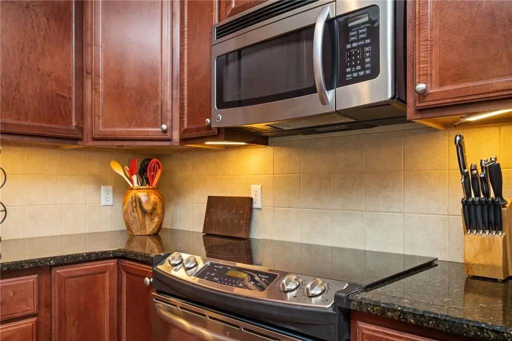 Kitchen featuring dark stone countertops, tasteful backsplash, and appliances with stainless steel finishes