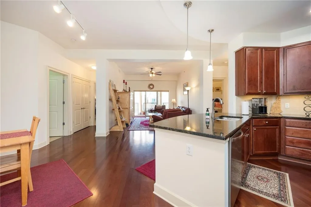 Kitchen featuring dark wood-type flooring, a ceiling fan, a sink, dark stone counters, and decorative backsplash