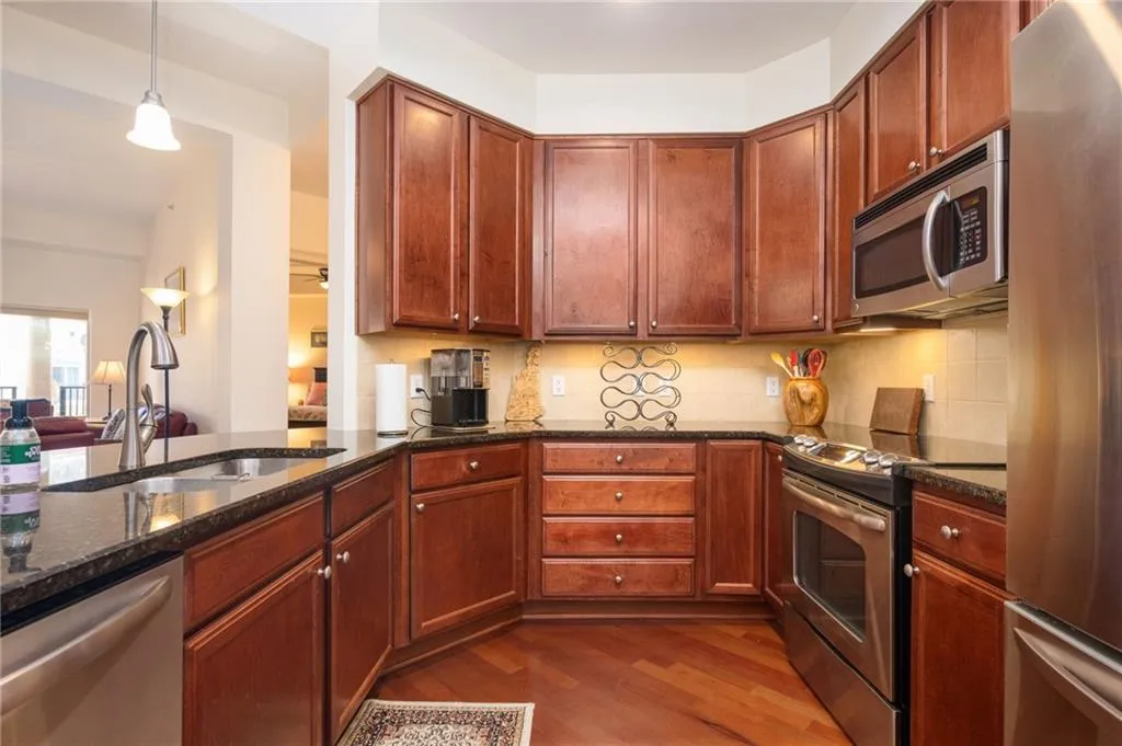 Kitchen with a sink, dark stone countertops, dark wood-style floors, stainless steel appliances, and decorative backsplash