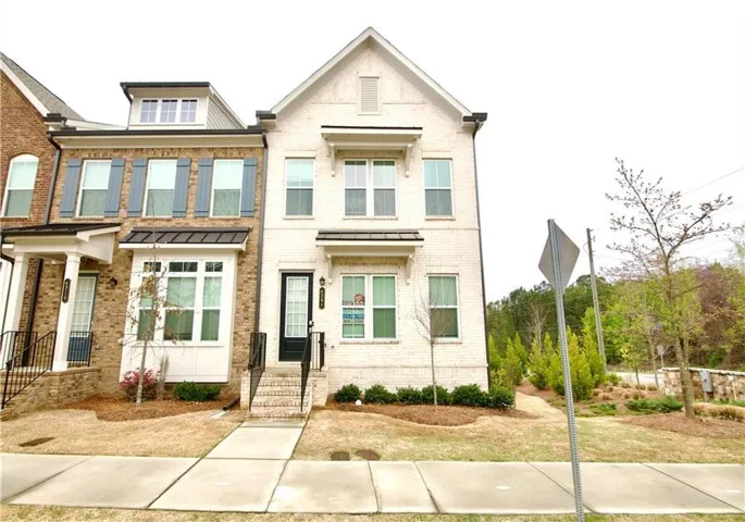 Three-story exterior with light brick finish, black framed front door, and a concrete walkway
