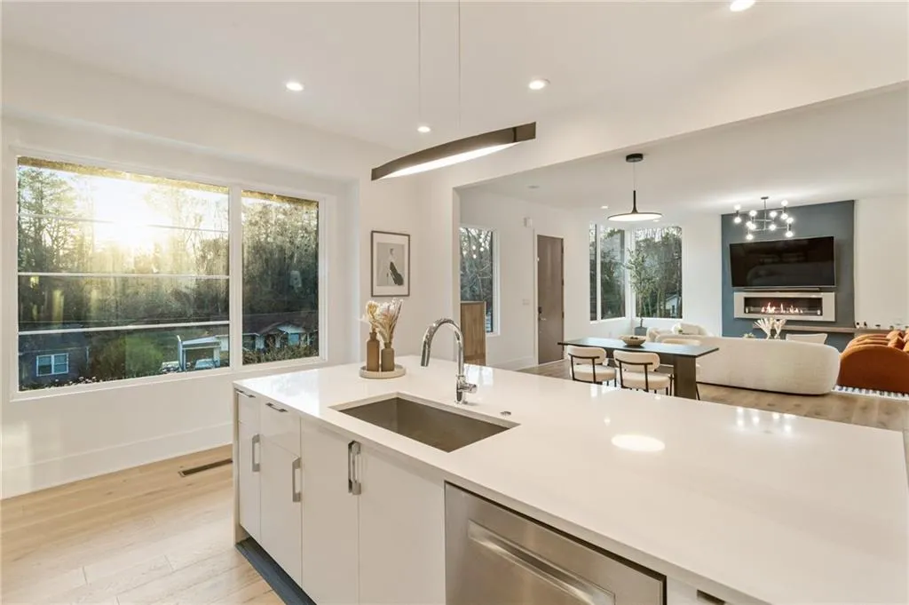 Kitchen with a sink, stainless steel dishwasher, open floor plan, white cabinetry, and light countertops