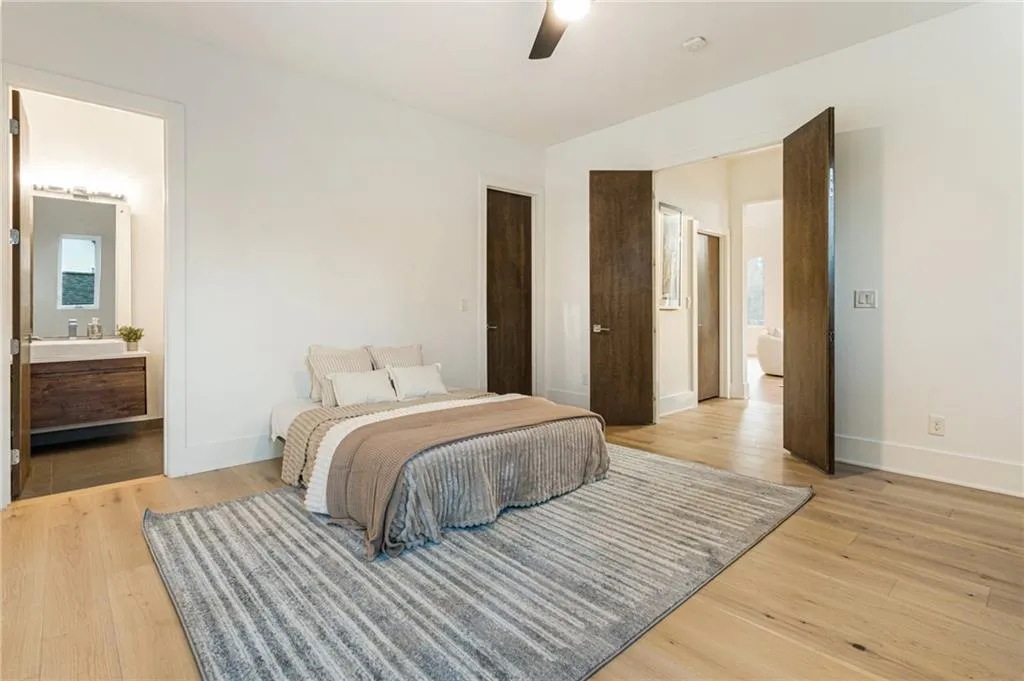 Bedroom with light wood finished floors, baseboards, ensuite bath, and ceiling fan