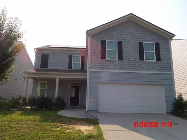 Two-story exterior featuring a covered front porch, a two-car garage, and solar panels on the roof
