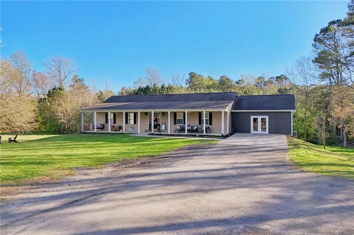 Ranch-style residence featuring a full-length covered porch with white columns, a large grass lawn, and a paved driveway