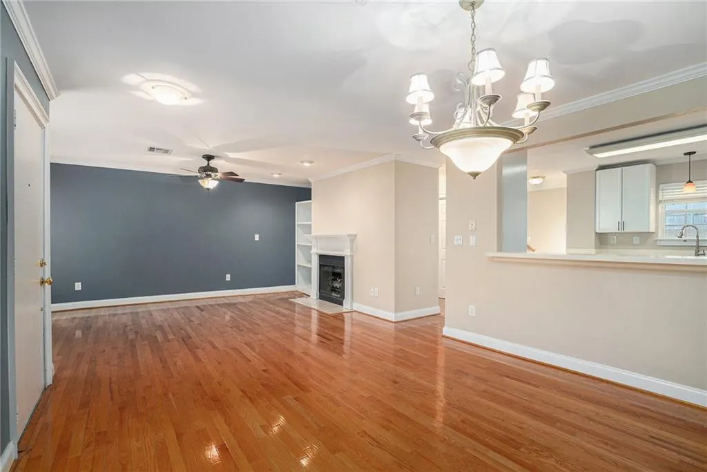 Unfurnished living room with ceiling fan with notable chandelier, crown molding, and light wood-type flooring