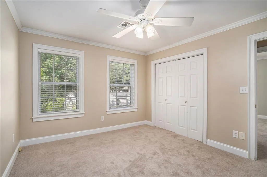 Unfurnished bedroom featuring a closet, light carpet, ornamental molding, and ceiling fan