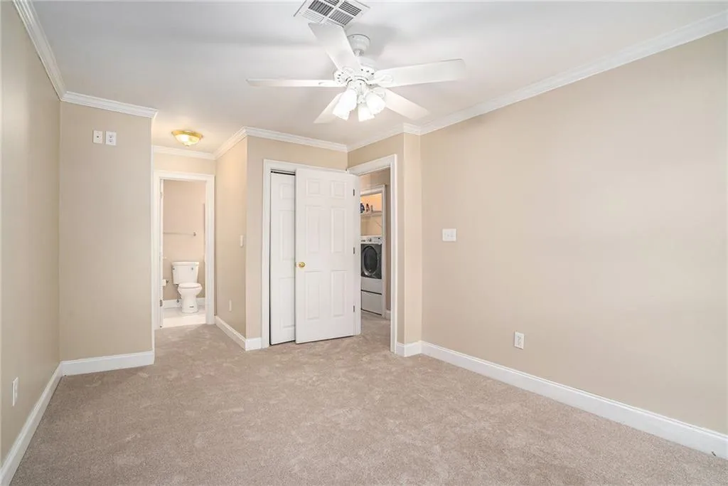 Unfurnished bedroom with connected bathroom, ceiling fan, ornamental molding, light carpet, and washer / clothes dryer