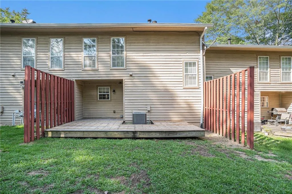 Back of house with central AC unit, a deck, and a lawn