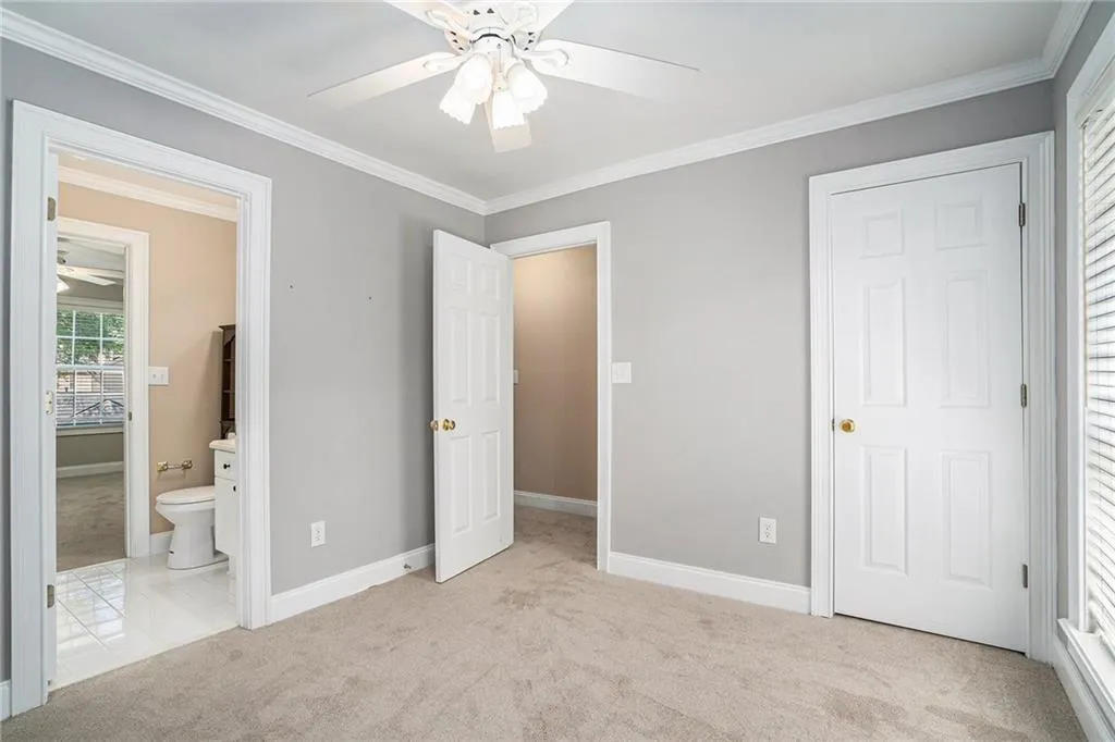 Unfurnished bedroom featuring ornamental molding, light carpet, ensuite bathroom, and ceiling fan