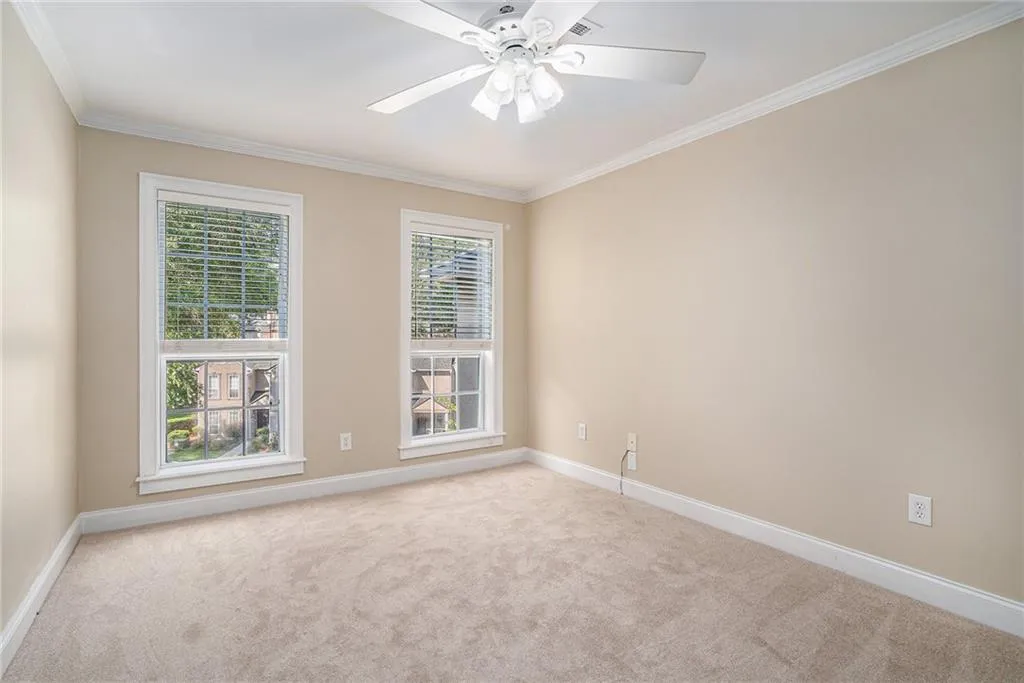 Carpeted empty room featuring plenty of natural light, ceiling fan, and ornamental molding