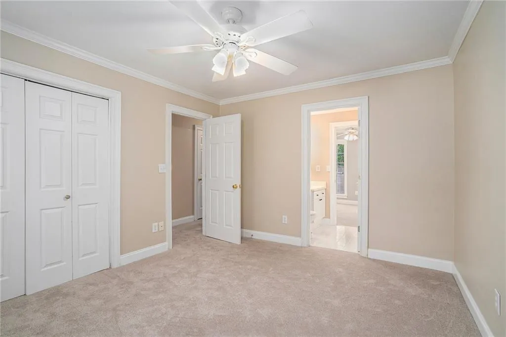 Unfurnished bedroom featuring ensuite bathroom, a closet, light colored carpet, crown molding, and ceiling fan
