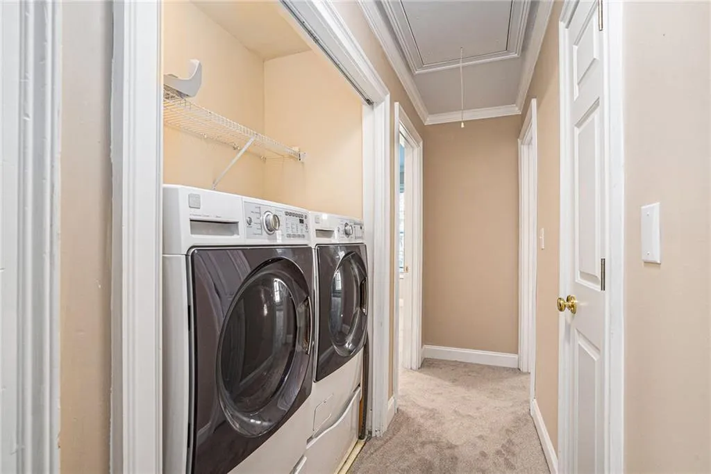 Laundry room featuring light carpet, washing machine and dryer, and ornamental molding