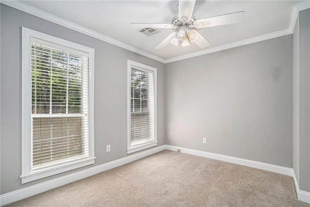 Carpeted spare room featuring ornamental molding, a wealth of natural light, and ceiling fan
