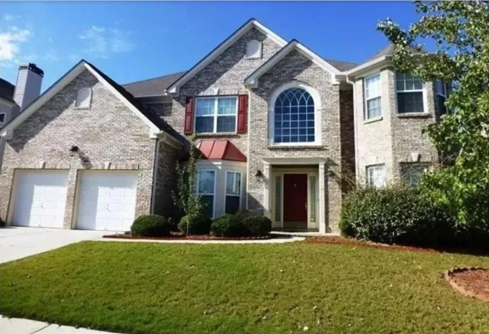 Brick exterior with a prominent arched window, a two-car garage, red accent shutters, and a landscaped front yard