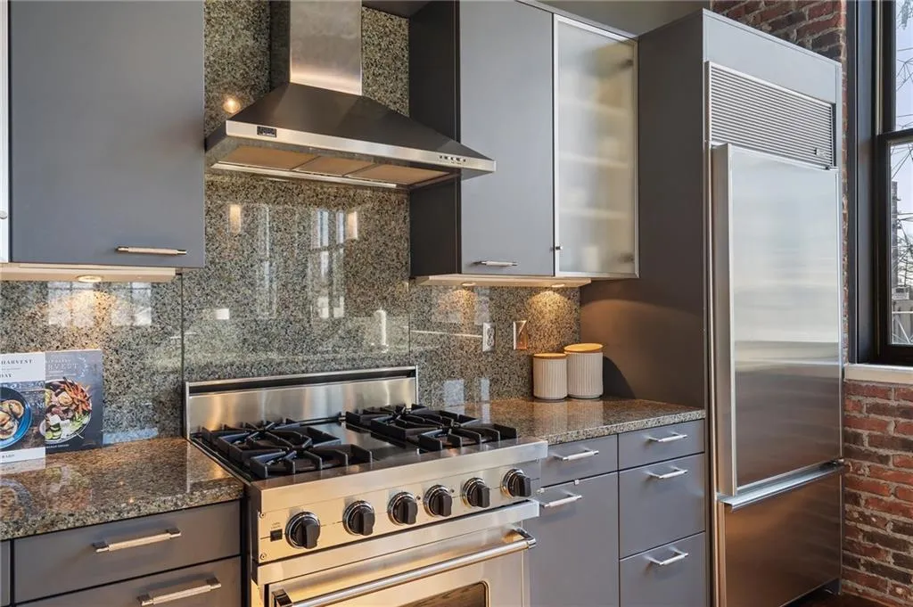 Kitchen featuring wall chimney range hood, gray cabinets, dark stone countertops, tasteful backsplash, and premium appliances