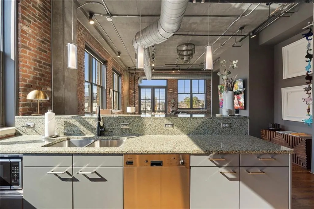 Kitchen featuring sink, appliances with stainless steel finishes, light stone countertops, brick wall, and dark hardwood / wood-style flooring