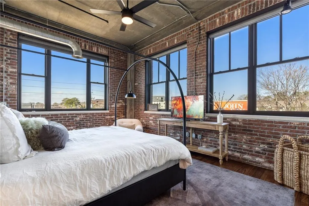 Bedroom featuring multiple windows, brick wall, and wood-type flooring