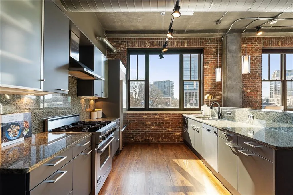 Kitchen with dark stone countertops, stainless steel stove, and brick wall