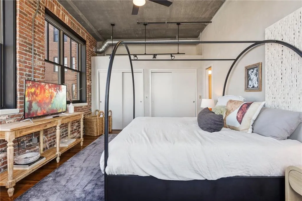 Bedroom with brick wall, dark wood-type flooring, and a towering ceiling