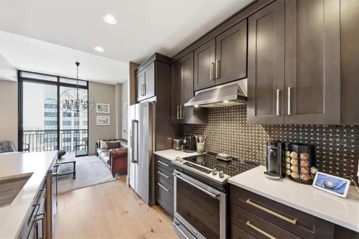 Kitchen with stainless steel appliances, suspended lighting, expansive windows, dark wood finish cabinets, and light wood-style flooring