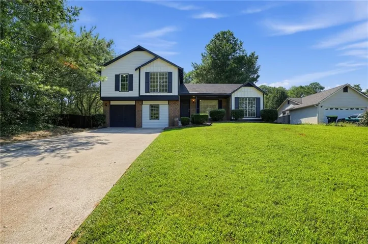 Two-story residence featuring white siding, dark blue shutters, brick accents, a two-car garage, and a concrete driveway