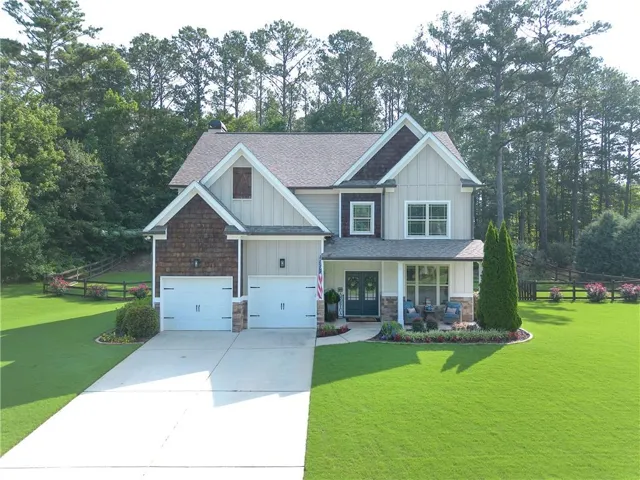 Craftsman-style home featuring a two-car garage, covered front porch with stone accents, and varied facade materials including board and batten siding and shingle siding