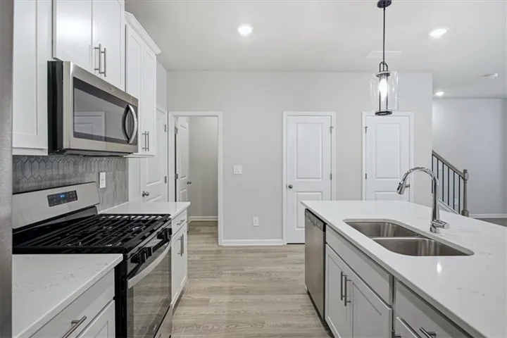 Modern kitchen featuring white shaker cabinetry, stainless steel appliances, a mosaic tile backsplash, and light wood-finish flooring