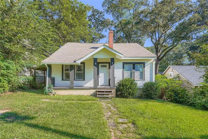 Bungalow-style home featuring a front lawn, a chimney, and a shingled roof