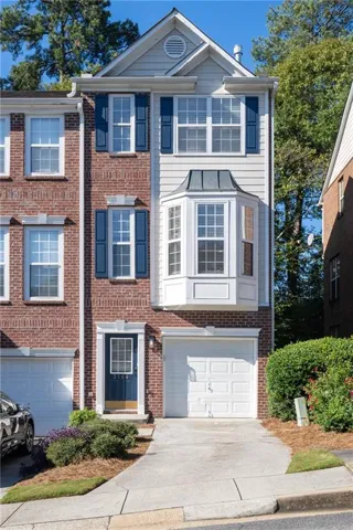Brick and siding exterior with a bay window, a gabled roofline, and a white garage door