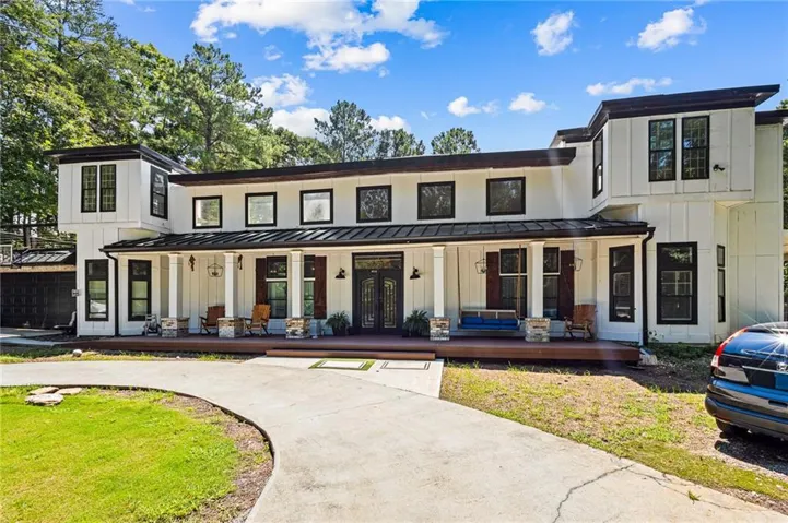 Modern farmhouse exterior with white board-and-batten siding, a dark metal roof, and a full-width covered porch with stone-accented columns