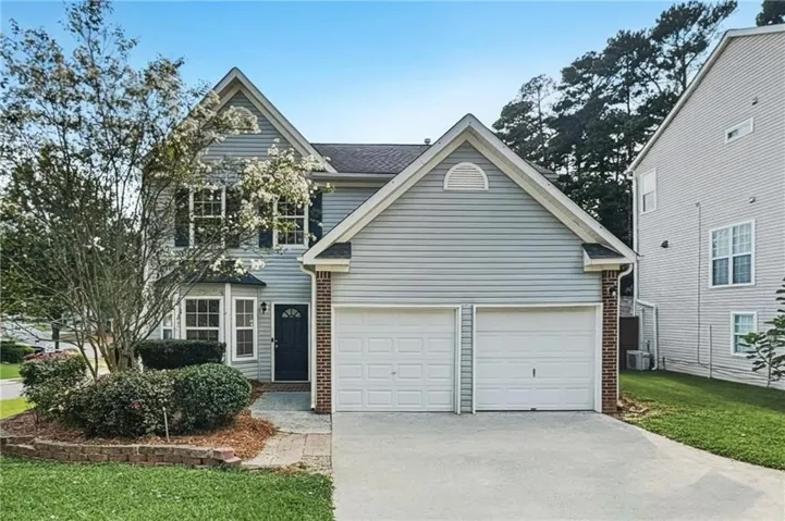 Two-story residence featuring light gray siding, brick accents, a two-car garage, and a concrete driveway