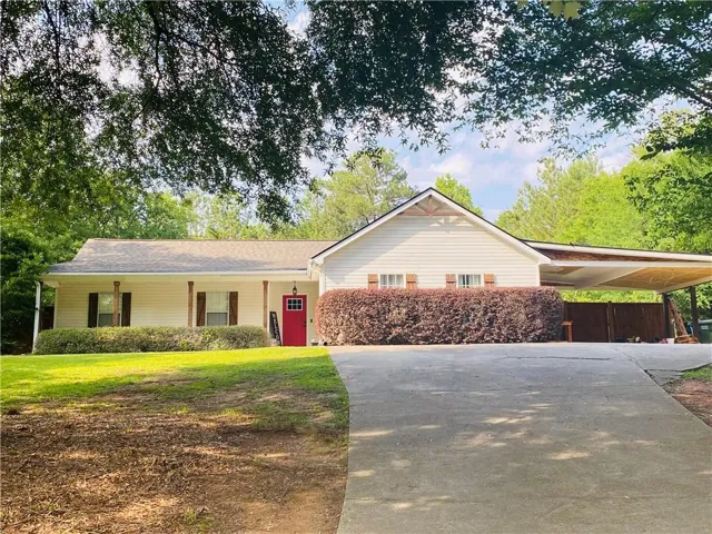 Siding exterior with a red front door, covered front porch, and a carport