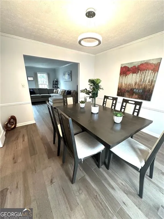 Dining room with a textured ceiling, wood finished floors, and crown molding