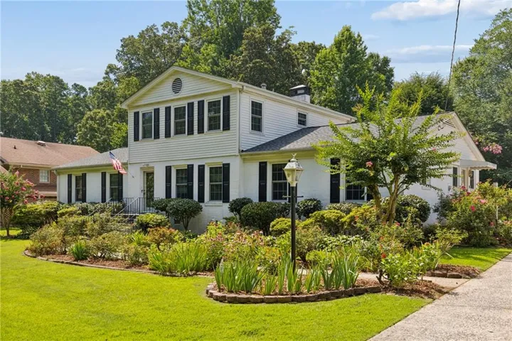 Two-story white exterior with dark shutters, featuring a prominent front entrance with stairs and a wrought iron railing