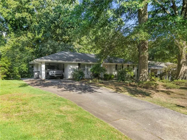 Single-story residence featuring a carport, a paved driveway, and mature trees providing natural shade