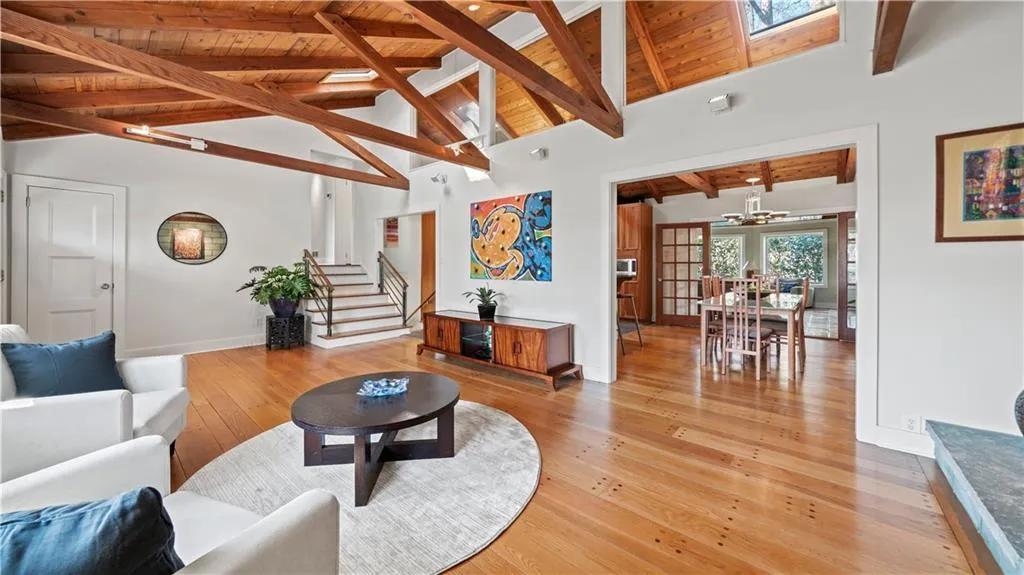 Living room featuring light hardwood / wood-style flooring, a skylight, a notable chandelier, high vaulted ceiling, and beam ceiling
