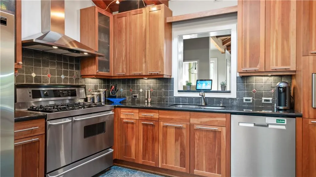 Kitchen with sink, appliances with stainless steel finishes, backsplash, and wall chimney exhaust hood