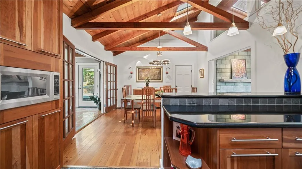 Kitchen featuring a notable chandelier, beamed ceiling, hanging light fixtures, a skylight, and stainless steel microwave