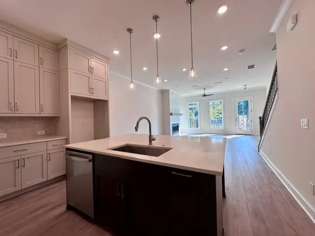 Kitchen island with undermount sink and stainless steel faucet, light-toned cabinetry, light wood-finish flooring, recessed lighting, and pendant lighting