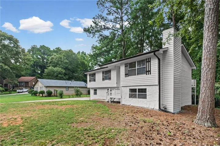 Split-level home featuring white siding, a prominent chimney, and dark window shutters