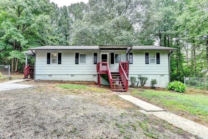Ranch-style residence featuring light-colored siding, black window shutters, and a covered entry with red-stained stairs