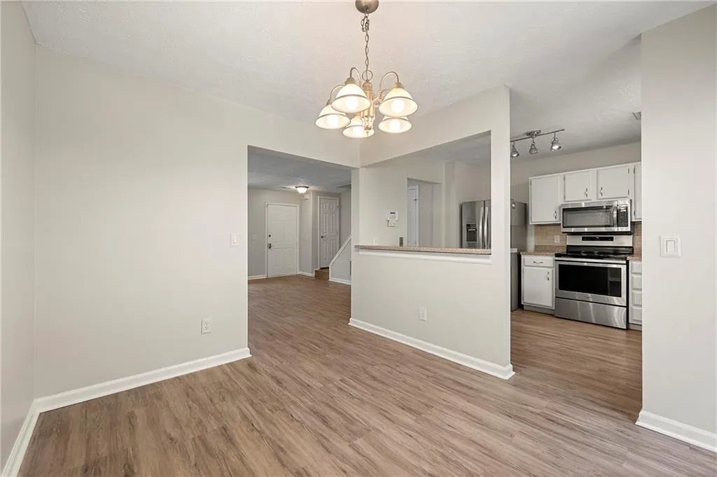 Kitchen featuring a chandelier, light wood-style flooring, stainless steel appliances, white cabinetry, and baseboards