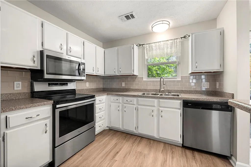 Kitchen with visible vents, decorative backsplash, appliances with stainless steel finishes, light wood-style floors, and a sink
