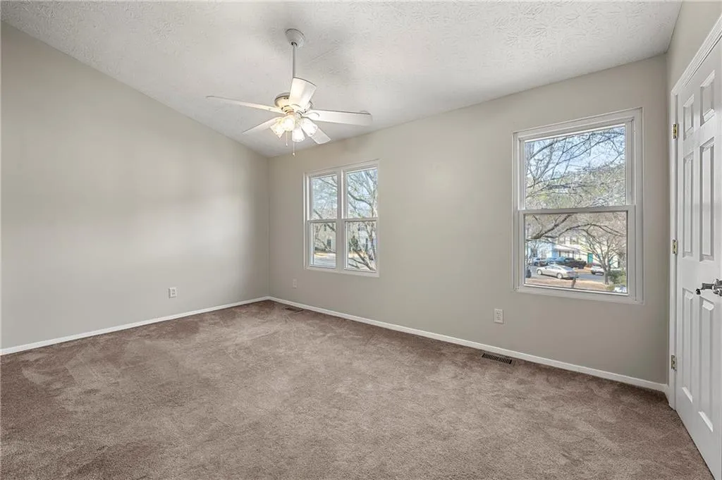 Carpeted spare room with vaulted ceiling, plenty of natural light, visible vents, and a ceiling fan